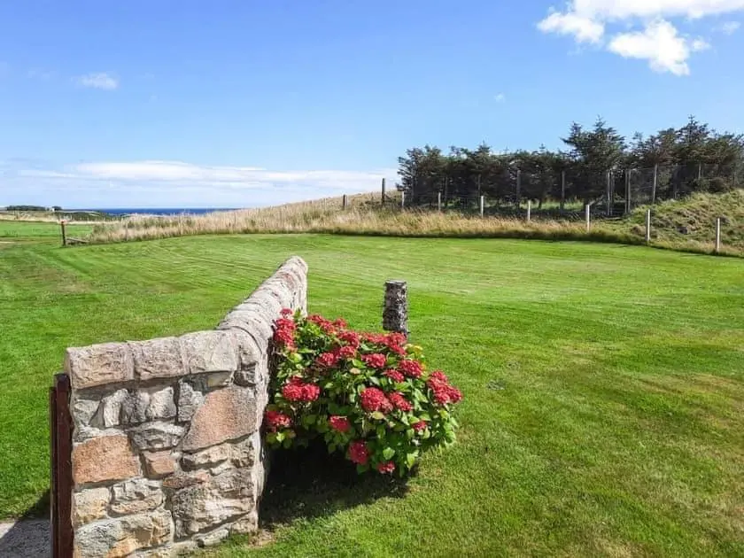 a stone wall with flowers in a field at Auld House in Brora