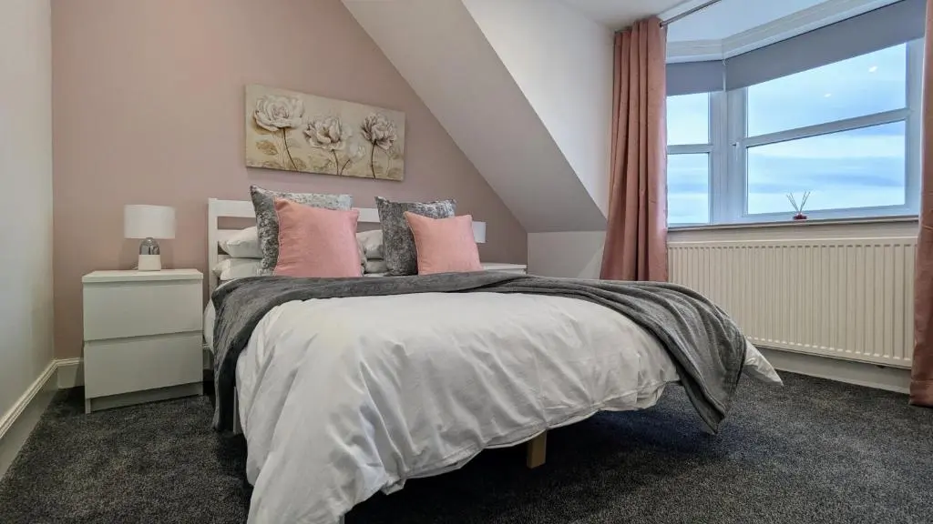 a bedroom with a bed with pink pillows and a window at The Wee Heilan' Dram in Keith