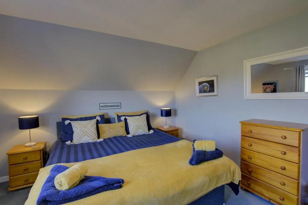 a bedroom with a large bed with blue sheets and pillows at Beach Croft, Brora in Brora