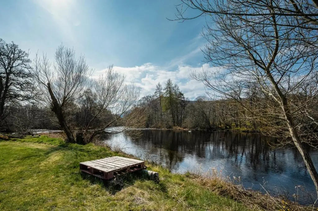 a wooden bench sitting in the grass next to a river at 2 Bed Chalet - Sleeps 4 - River and mountain views in Strathpeffer