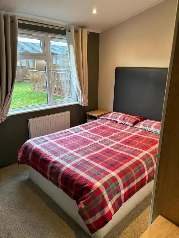 a bedroom with a bed with a plaid blanket and a window at Hepburns Lodge 19 in Strachan