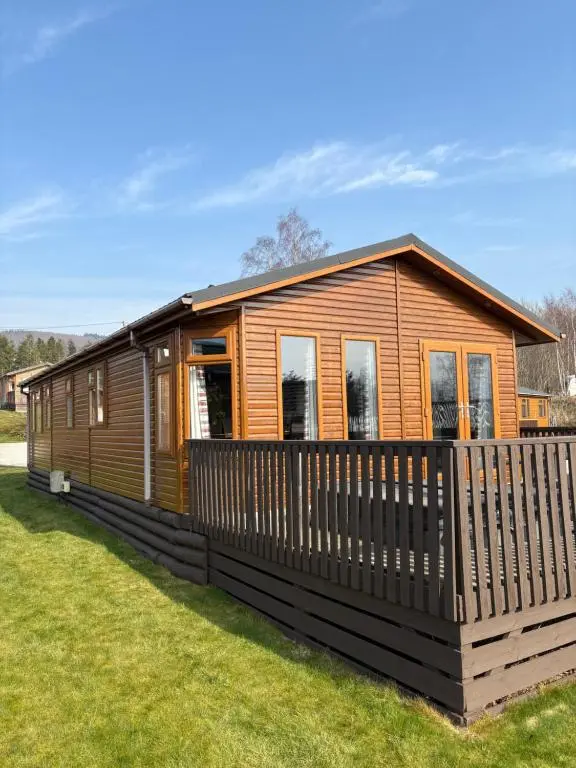 a wooden cabin with a fence in the grass at Hepburns Lodge 19 in Strachan