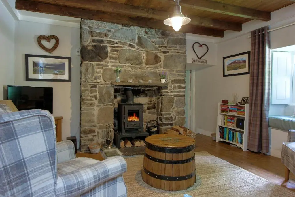 a living room with a stone fireplace with a barrel at Bridge Cottage in Glenlivet
