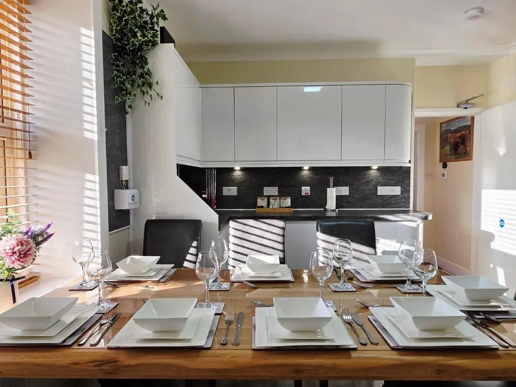 a wooden table with white plates and wine glasses at Inverness City 4 Bedroom house free parking in Inverness
