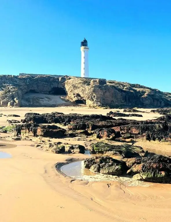 a lighthouse on top of a hill with a beach at Silver Dunes in Lossiemouth