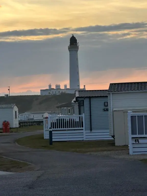 a lighthouse with a building and a house with a fence at Silver Dunes in Lossiemouth