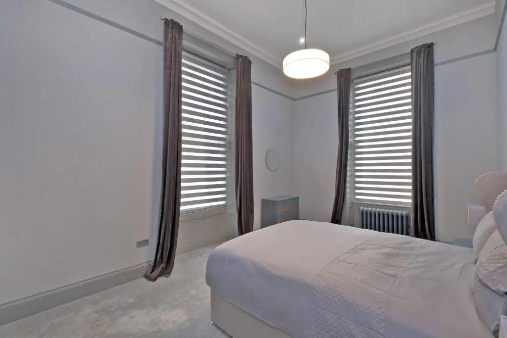 a white bedroom with a bed and two windows at Kirkton House in Kirkton of Skene