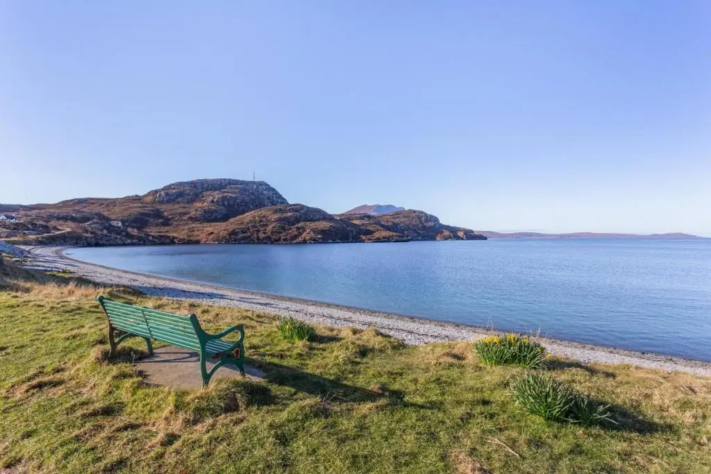 a green bench sitting on the side of a beach at 3 Bed in Strathkanaird oc-r30948 in Ullapool