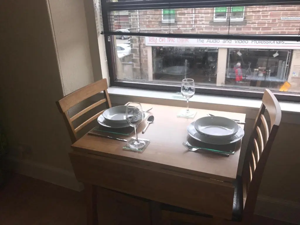 a wooden table with plates and glasses and a window at Butterfly Apartment in Inverness