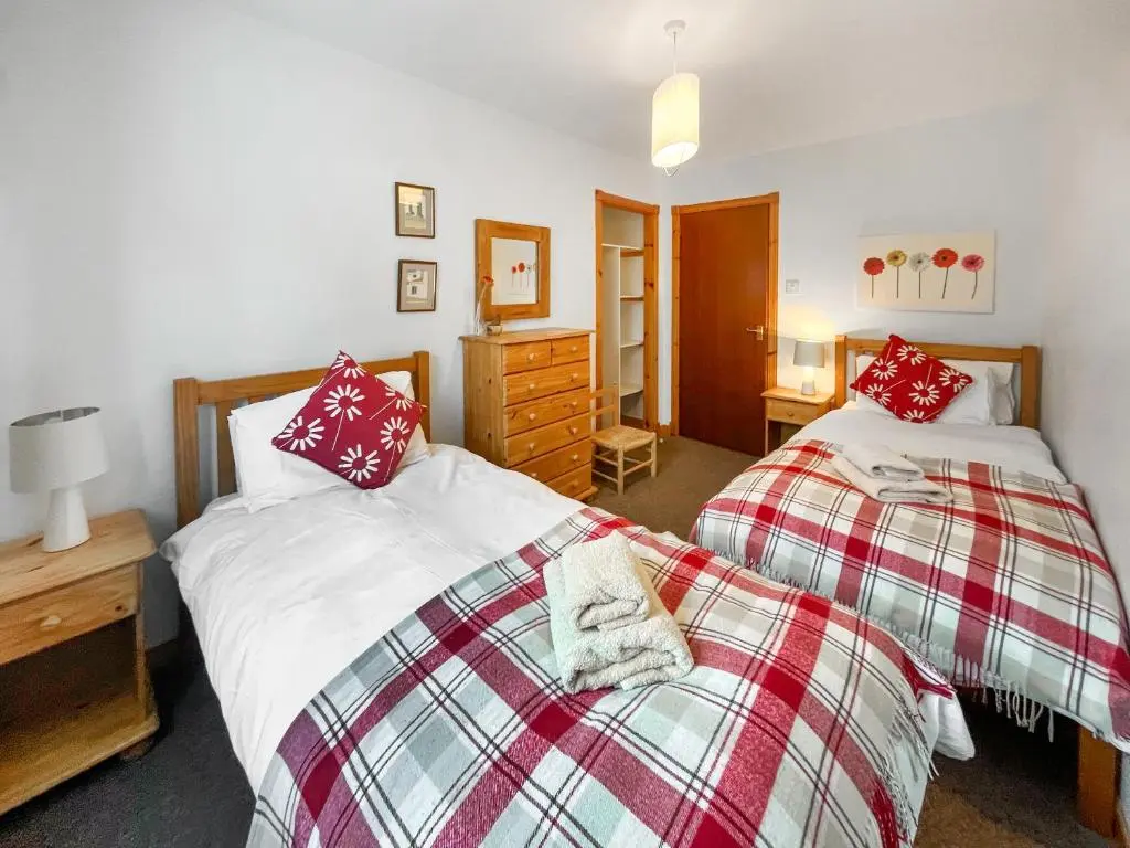 a bedroom with two beds and a dresser at Heath Cottage in Boat of Garten
