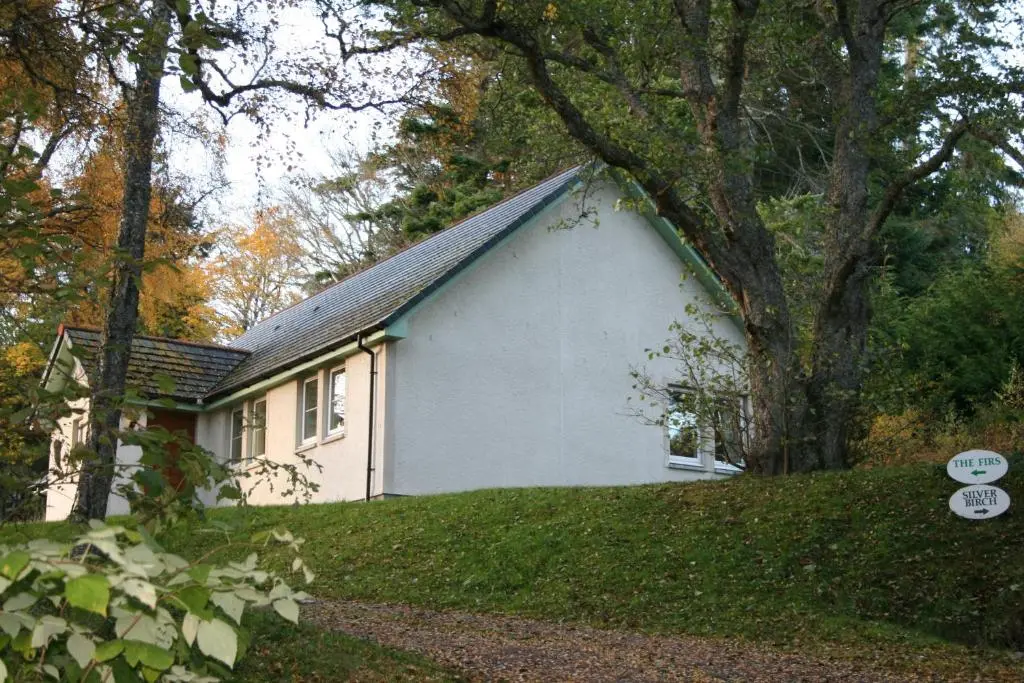 a white house with a black roof in the grass at BCC Loch Ness Cottages in Drumnadrochit