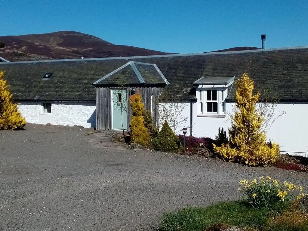 a white house with a door and trees in front of it at Coo Shed in Glenshee