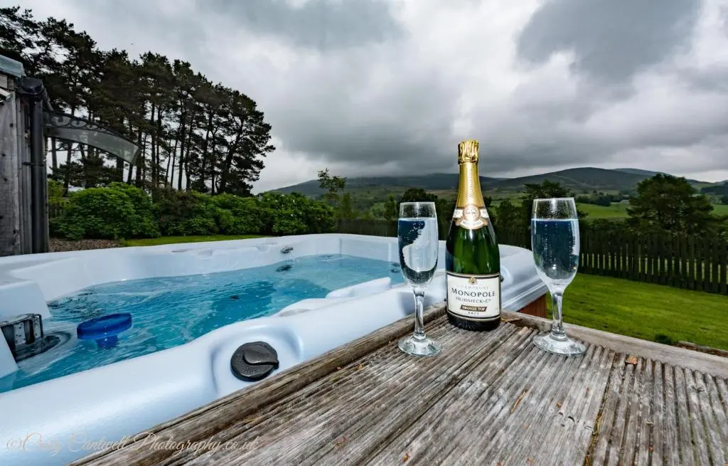 a bottle of champagne and two glasses on a table next to a tub at Coo Shed in Glenshee
