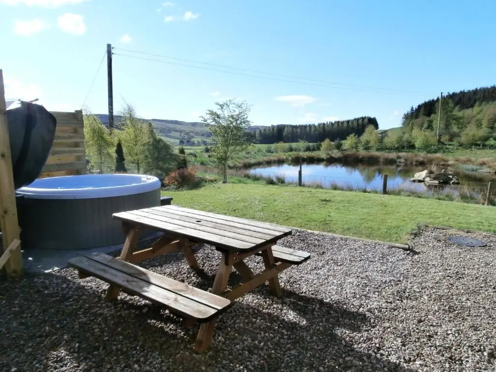 a wooden picnic table sitting next to a pond at Smiddy Cottage in Glenshee