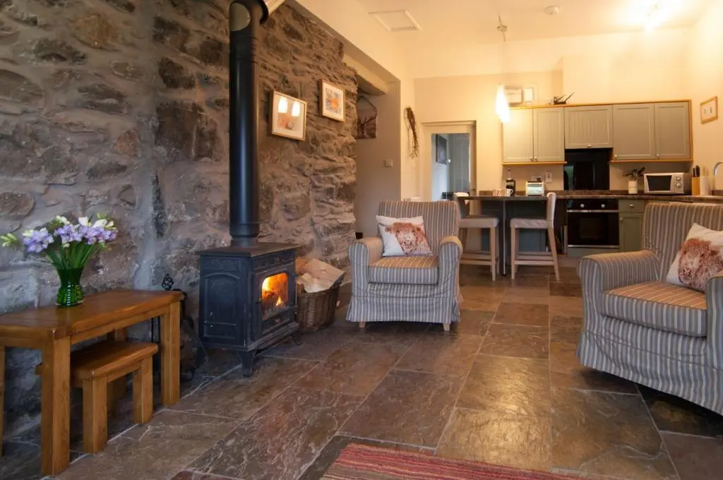 a living room with a wood stove and chairs at Smiddy Cottage in Glenshee