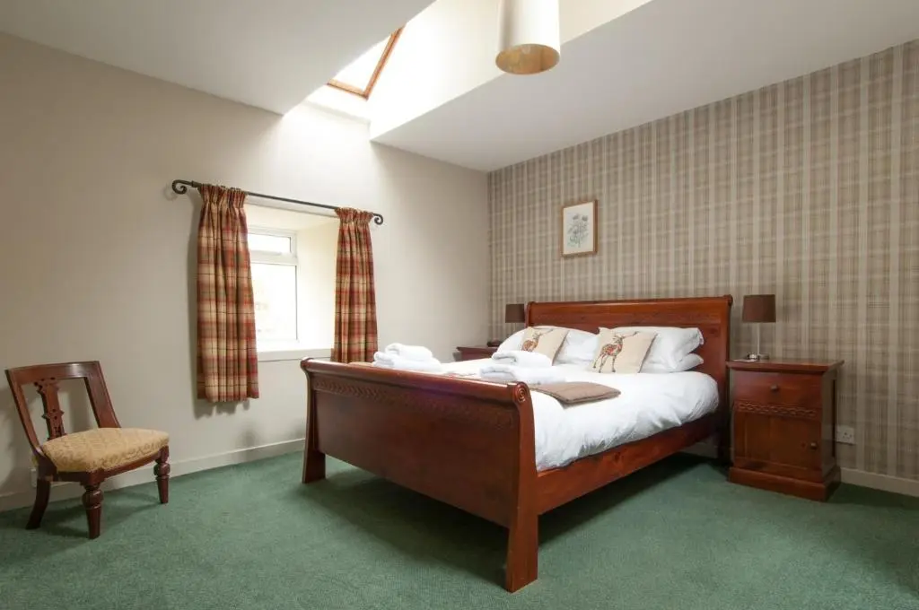 a bedroom with a bed and a chair and a window at Smiddy Cottage in Glenshee