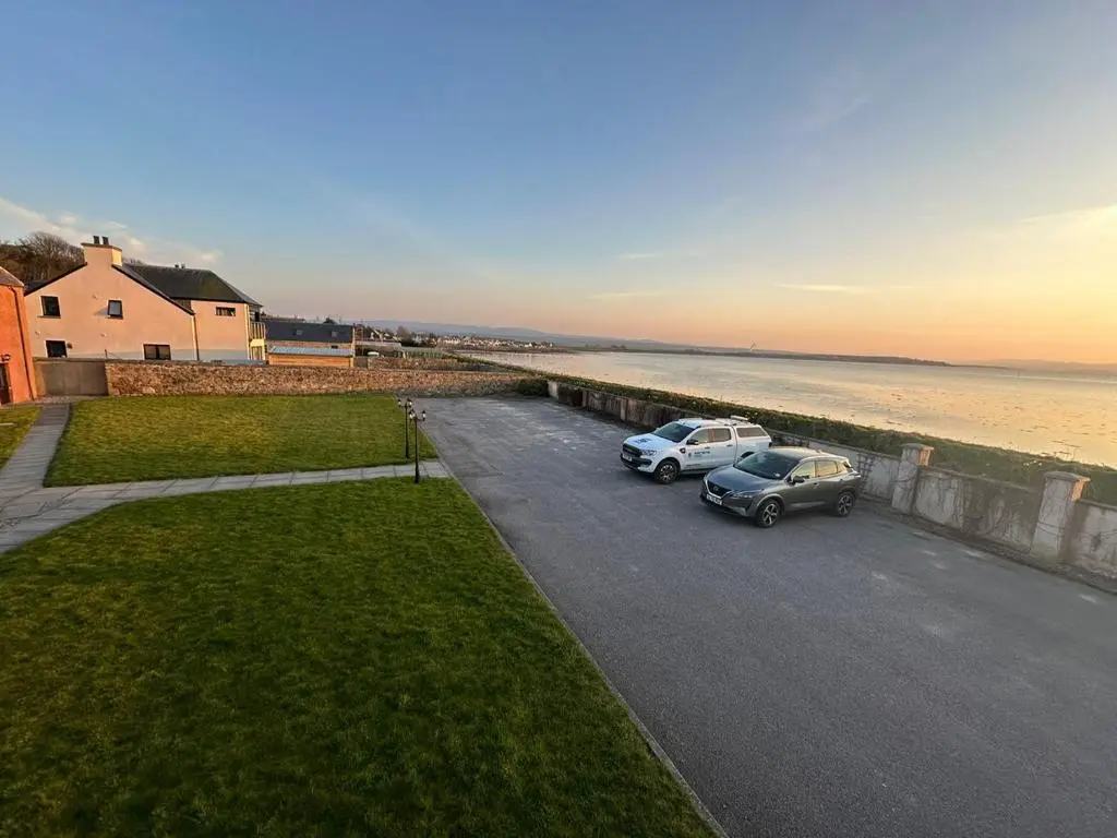 two cars parked in a parking lot next to the ocean at Dolphin Bay Suites in Ardersier