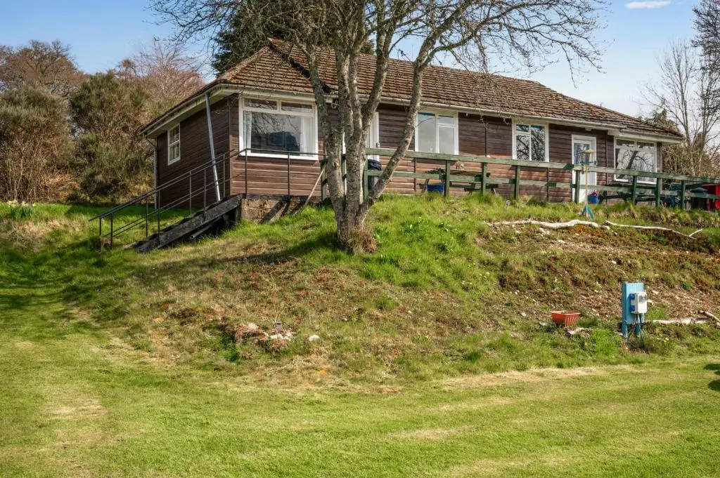a house on a hill with a tree in front at 2 Bed Chalet - Sleeps 3 - River and mountain views in Strathpeffer