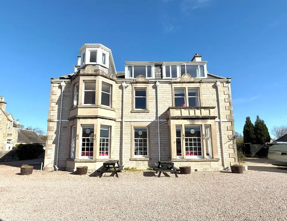 a large stone building with a bench in front of it at Seabank House Hotel in Nairn