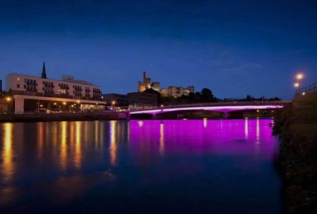 a bridge over a river at night with purple lights at Inverness City Centre Apartment! in Inverness