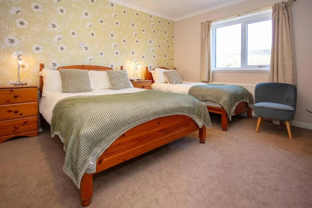 a bedroom with two beds and a window and a chair at Old Surgery Guest House in Ullapool