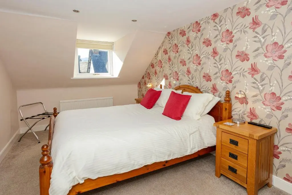 a bedroom with a bed with white sheets and red pillows at Old Surgery Guest House in Ullapool