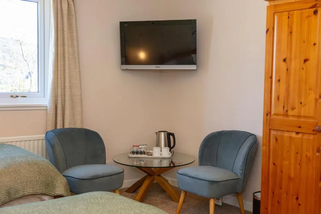 a room with two chairs and a table and a tv at Old Surgery Guest House in Ullapool