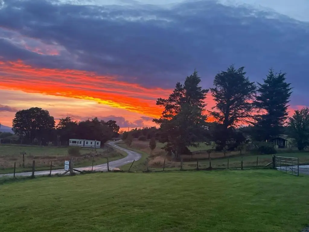 a sunset over a field with a road at Woodend Caravan in Shinness