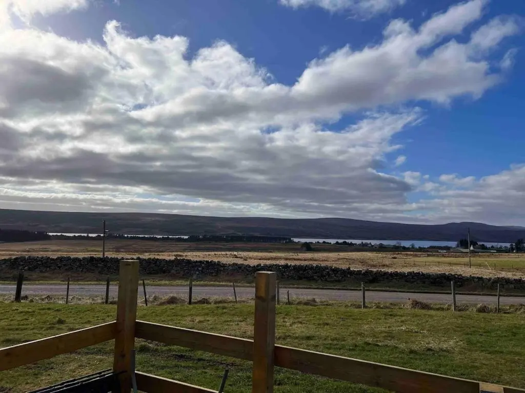 a field with a fence and a sky with clouds at Woodend Caravan in Shinness