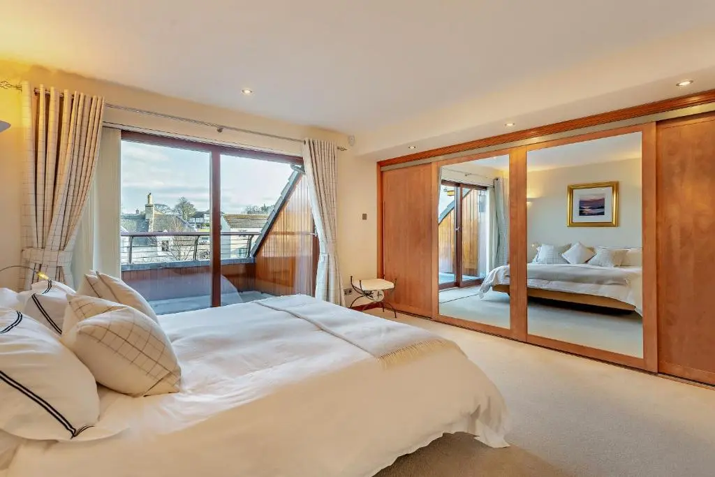 a bedroom with a large white bed and a balcony at Penthouse Golf View Apartments in Lossiemouth
