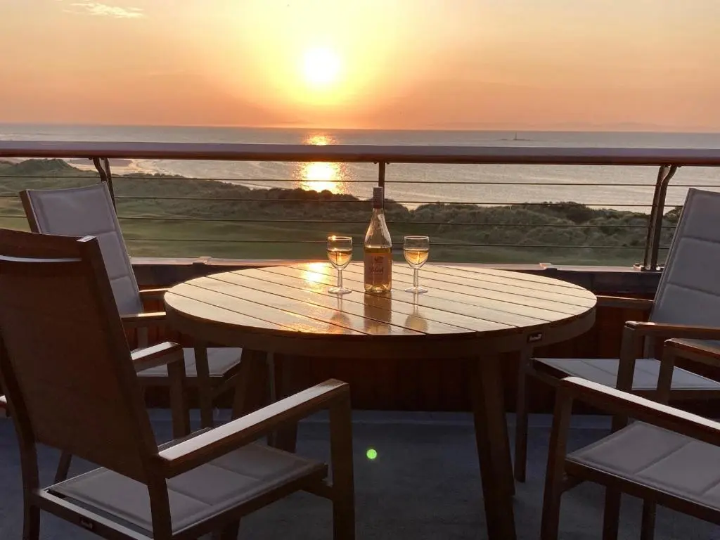 a table with two wine glasses on a balcony with the sunset at Penthouse Golf View Apartments in Lossiemouth