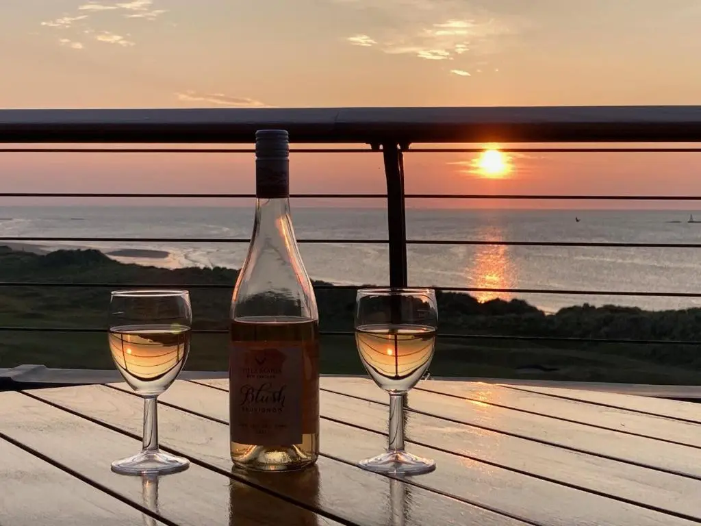 a bottle of wine and two glasses on a table with the sunset at Penthouse Golf View Apartments in Lossiemouth