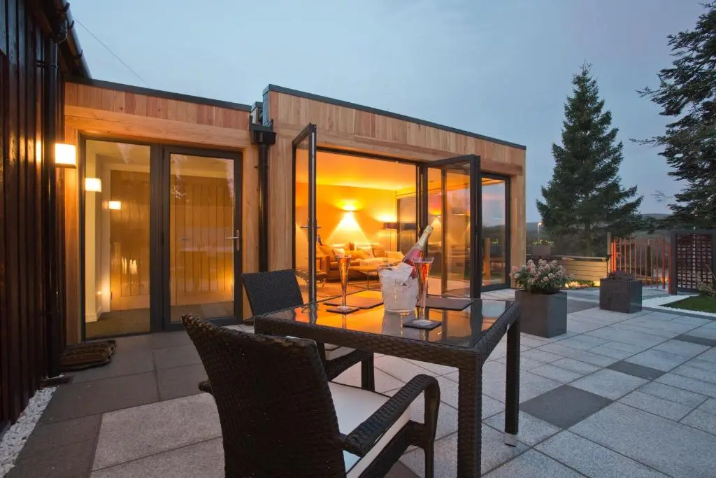 a house with a table and chairs on a patio at The Invergarry - Royal Deeside Luxury 5 star Couples Retreat with Hot Tub, Aboyne in Aboyne