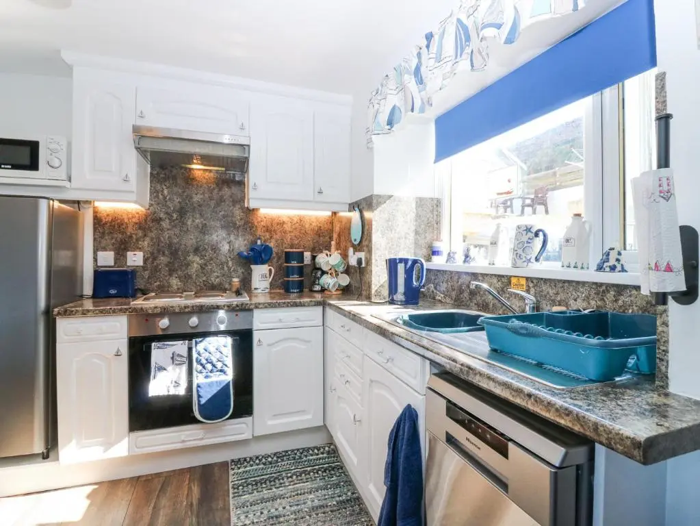 a kitchen with white cabinets and a blue sink at Periwinkle Cottage in Banff