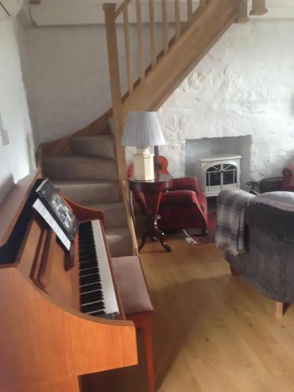 a living room with a staircase and a piano at The Hoose in Helmsdale