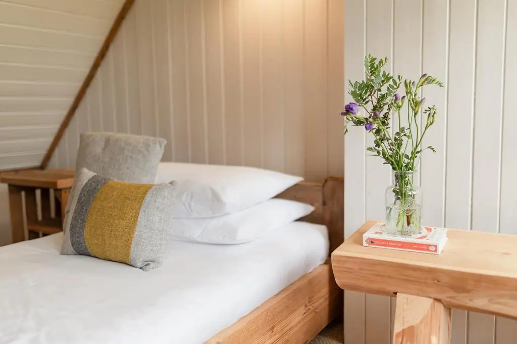 a bed with a vase of flowers on a table at Broomfeild Bothy Comes with a Sauna in Boat of Garten