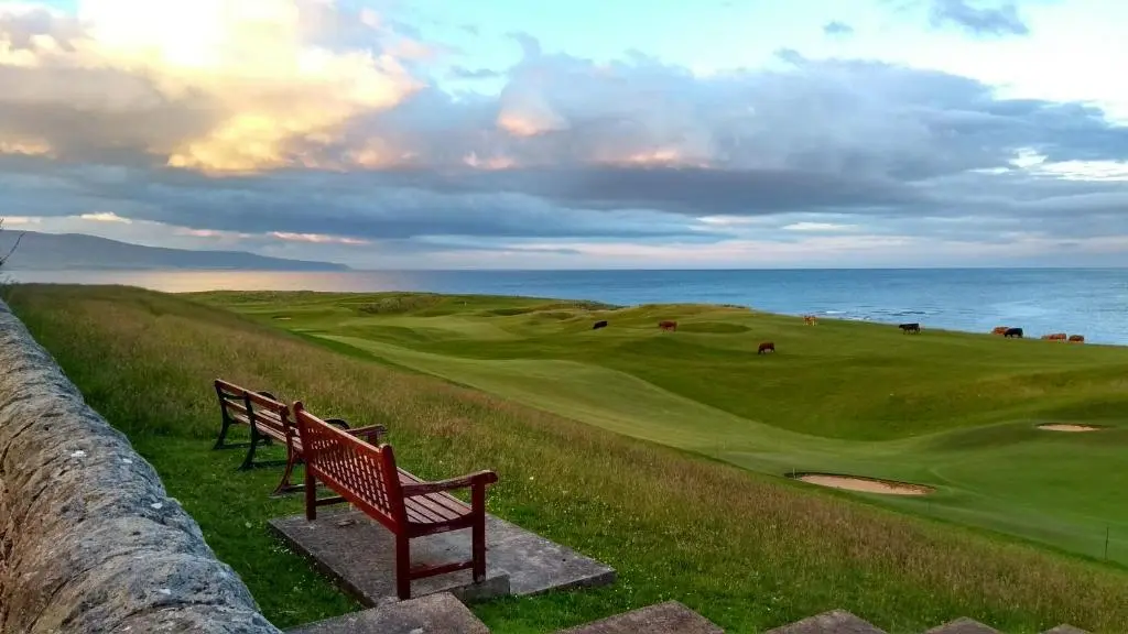 two benches sitting on a hill next to the ocean at Dalchalm Hideaway in Brora