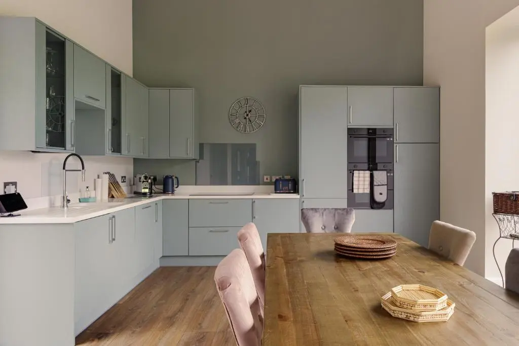 a kitchen with a wooden table and white cabinets at Elrick Estate - Coach House in Newmachar