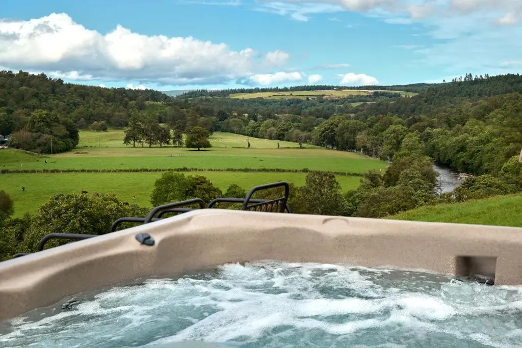 a hot tub with a view of a river and trees at Old Manse of Craggan in Glenlivet