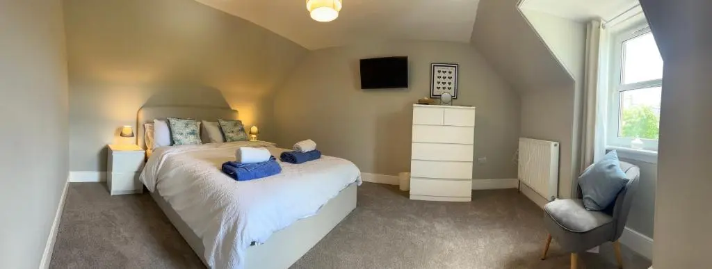 a bedroom with a bed with blue pillows and a chair at 2 Links Place in Nairn