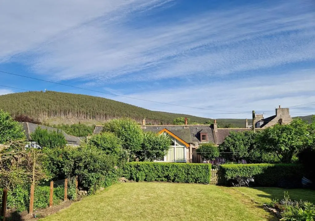 a garden with a house and a hill in the background at Spacious cosy welcoming cottage in Ballater