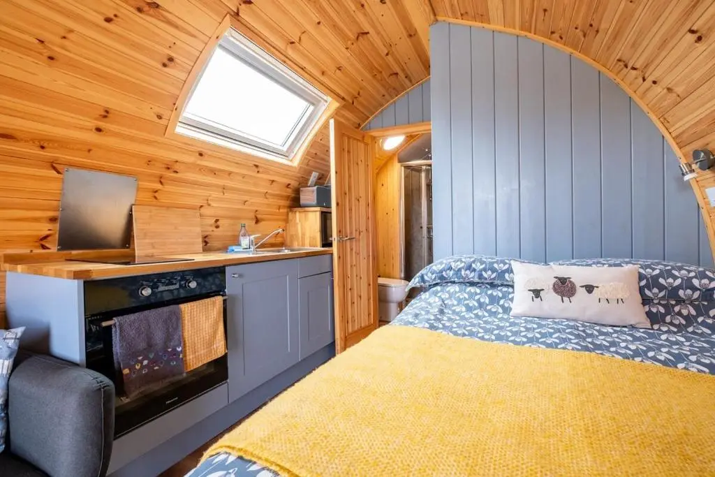 a bedroom with a bed and a kitchen in a cabin at Luxury Pod 3 in Bonar Bridge