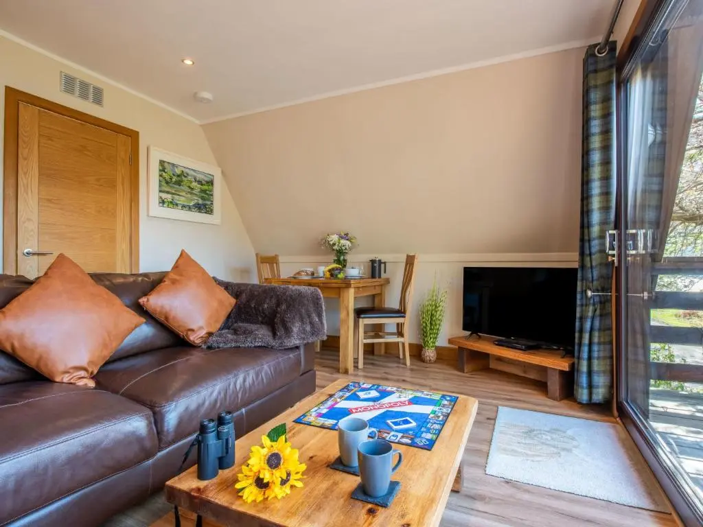 a living room with a brown leather couch and a table at Chalet Sandpiper Lodge by Interhome in Spean Bridge