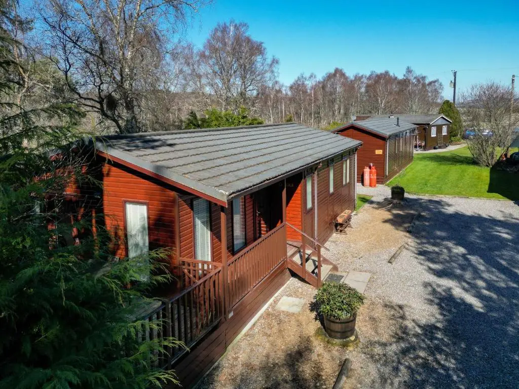 a log cabin with a black roof and a yard at Chalet Lodge 7 by Interhome in Boat of Garten