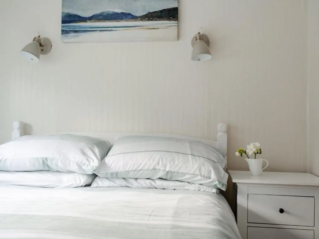 a bed with white sheets and a painting on the wall at Chalet Lodge 8 by Interhome in Boat of Garten