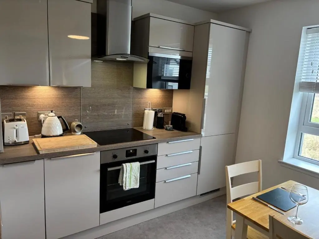 a kitchen with white appliances and a table and a dining room at Gorgeous Dornoch apartment in Dornoch