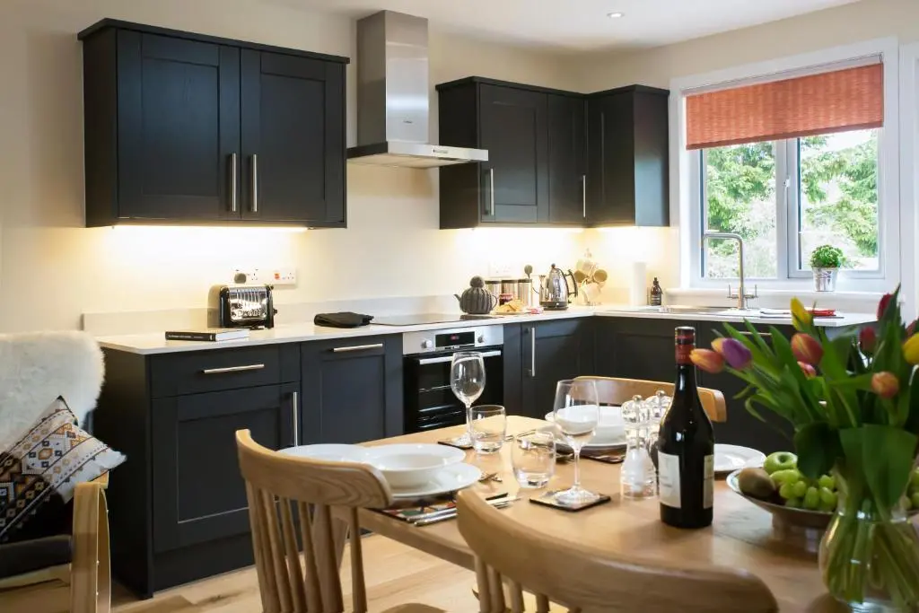 a kitchen with black cabinets and a table with wine glasses at Loch Cottage in Boat of Garten