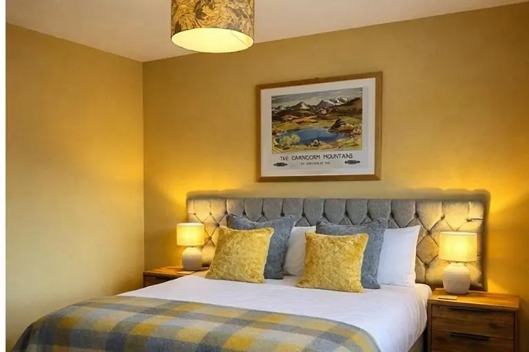 a bedroom with a large bed with yellow walls at Loch Cottage in Boat of Garten