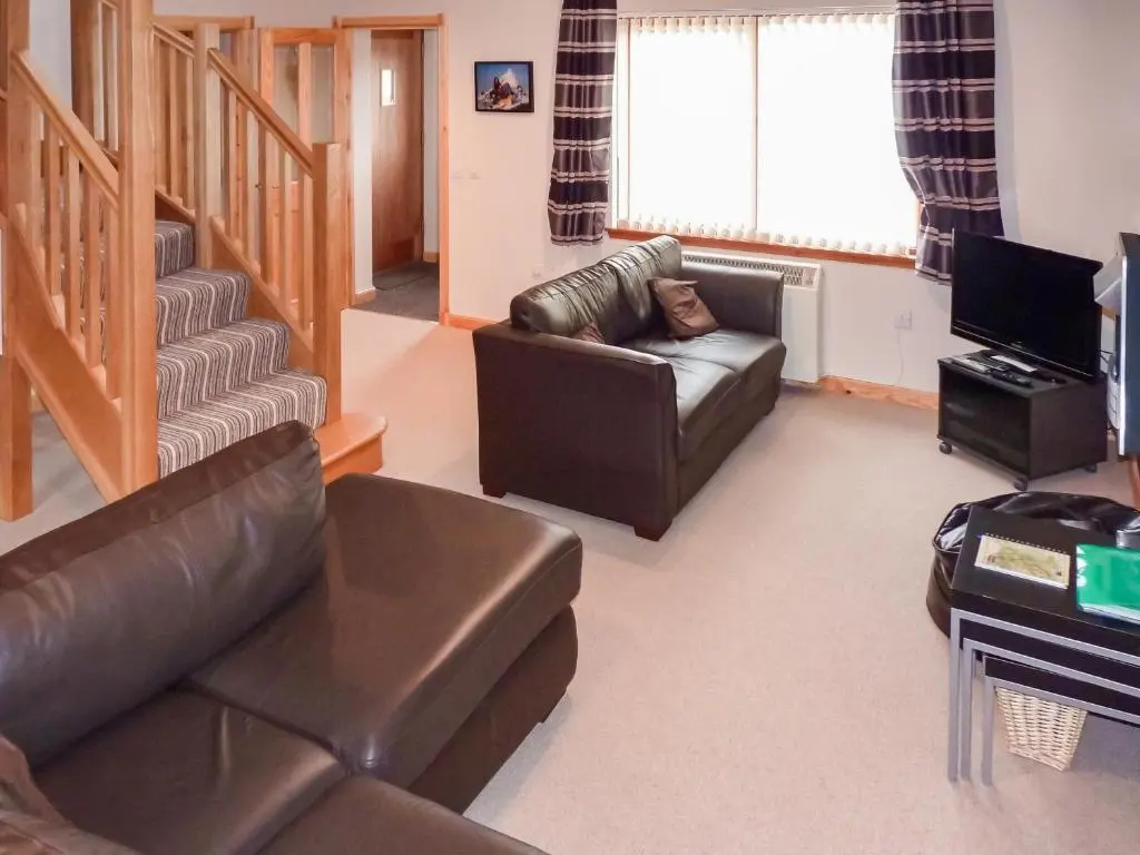 a living room with a leather couch and a television at Rowlands in Aviemore