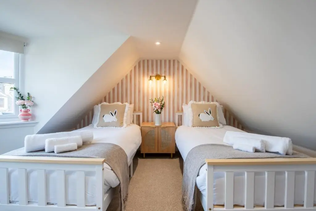 a attic bedroom with two beds and a staircase at Keel Cottage & Dog Friendly in Nairn